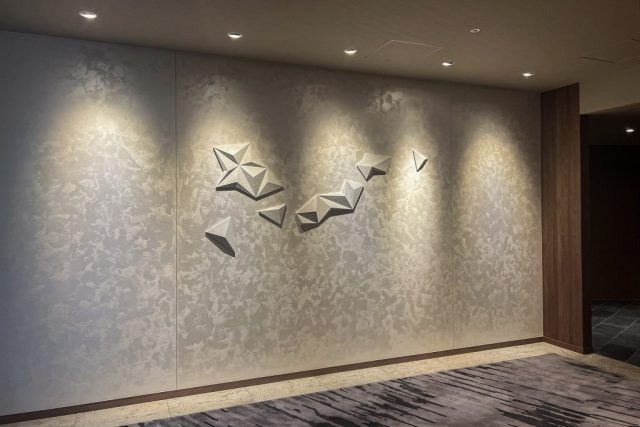 白い和紙でできたジオメトリックパターンの立体構成アート。白く輝く壁面に浮かび上がるホテルのエレベーターホールに設置された壁面装飾。