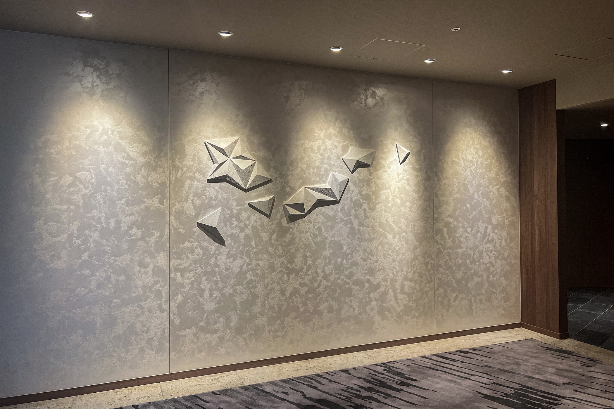 白い和紙でできたジオメトリックパターンの立体構成アート。白く輝く壁面に浮かび上がるホテルのエレベーターホールに設置された壁面装飾。